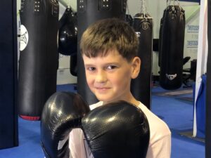 a boy smiling standing in a boxing gym wearing boxing gloves