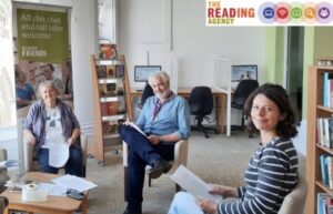 two ladies and a man sitting in a library reading 