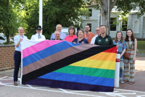 large rainbow flag being held up with people standing behind