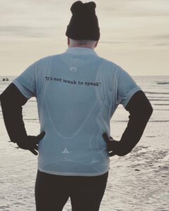 man looking out to sea with it's not weak to speak printed on the back of his tshirt