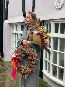 a lady in a grey coat holding a wreath of flowers